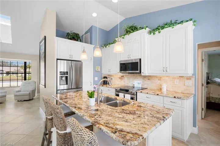 Kitchen featuring white cabinetry, stainless steel appliances, pendant lighting, light stone counters, and vaulted ceiling