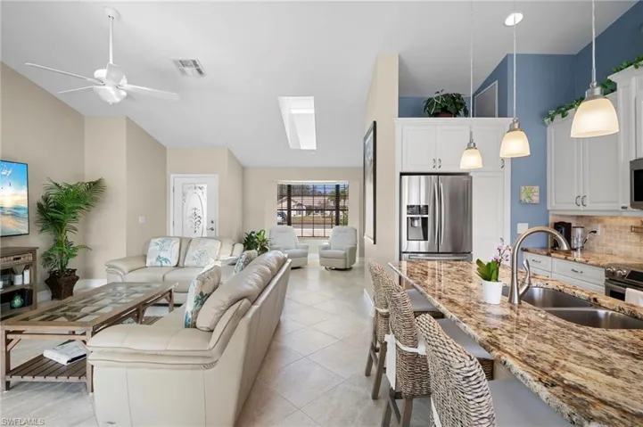 Living room featuring a skylight, lofted ceiling, light tile patterned flooring, and ceiling fan