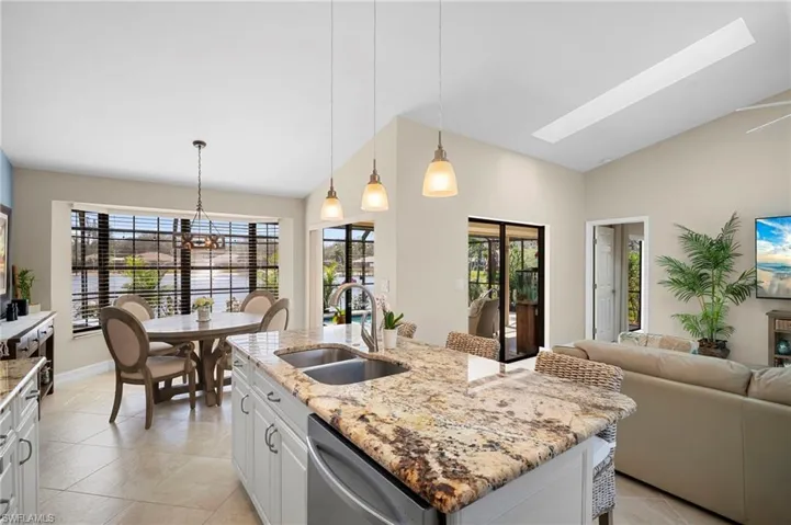 Kitchen featuring light stone countertops, decorative light fixtures, white cabinetry, a skylight, and vaulted ceiling