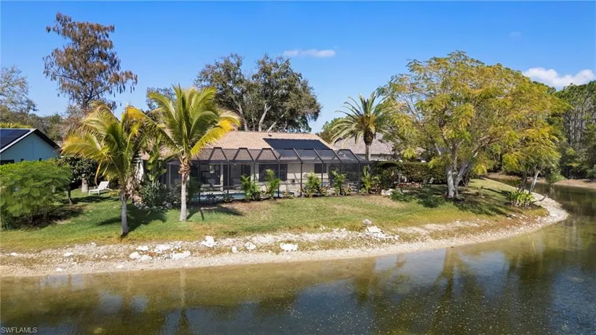 Rear view of house featuring glass enclosure, a sunroom, a lawn, and a water view