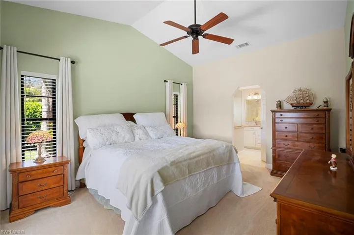 Bedroom with arched walkways, lofted ceiling, light colored carpet, a ceiling fan, and ensuite bath