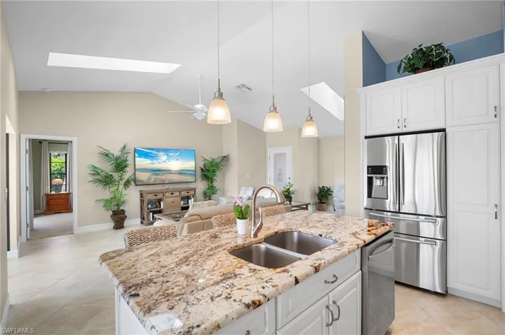 Kitchen featuring a skylight, white cabinetry, stainless steel appliances, decorative light fixtures, and a high ceiling