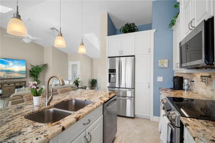 Kitchen featuring stainless steel appliances, hanging light fixtures, white cabinetry, light stone counters, and backsplash