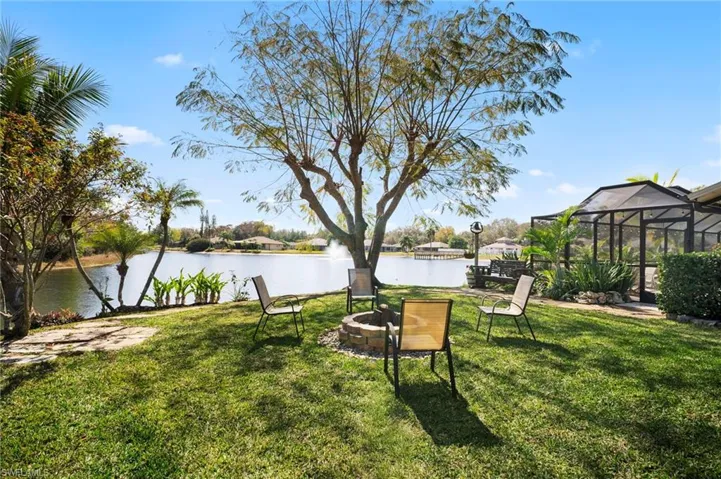 View of grassy yard with a water view, an outdoor fire pit, a patio area, and a lanai