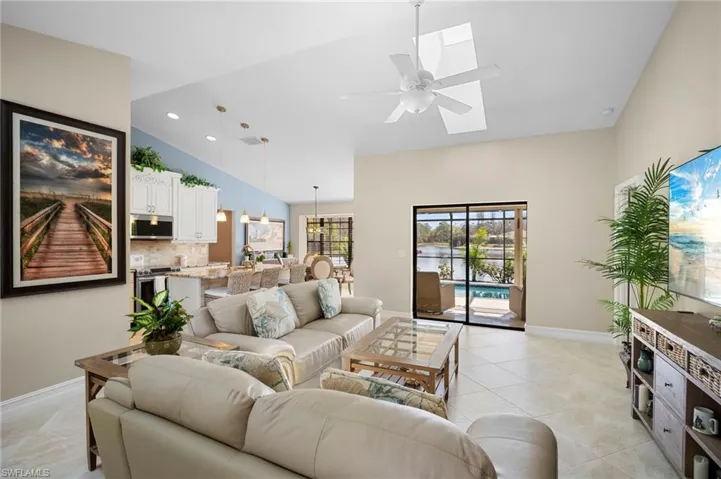Living area with vaulted ceiling, a ceiling fan, a skylight, light tile patterned flooring, and recessed lighting