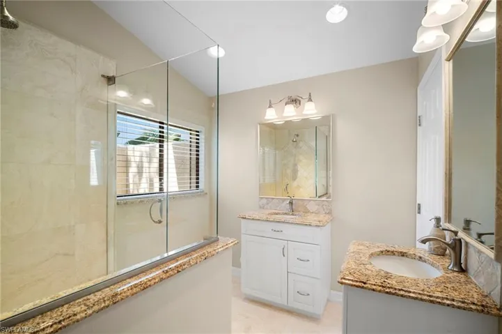 Full bathroom with a walk in shower, two vanities, and vaulted ceiling