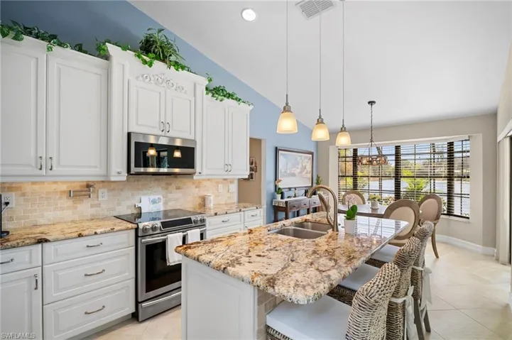 Kitchen with stainless steel appliances, white cabinetry, light stone countertops, a kitchen breakfast bar, and vaulted ceiling
