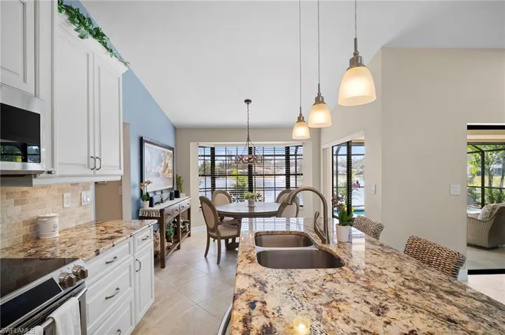 Kitchen with decorative light fixtures, stainless steel appliances, white cabinetry, light stone countertops, and lofted ceiling