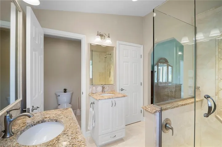 Bathroom featuring two vanities, a stall shower, and light tile patterned floors