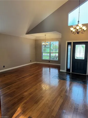 Foyer entrance featuring a chandelier, dark wood-style floors, healthy amount of natural light, and a high ceiling