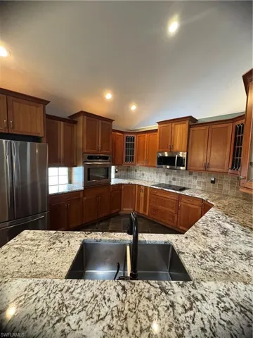 Kitchen featuring refrigerator, oven, light stone countertops, glass insert cabinets, and recessed lighting
