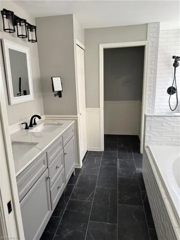 Bathroom with tiled bath, double vanity, wainscoting, and a tile shower