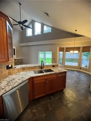 Kitchen featuring high vaulted ceiling, a peninsula, dishwasher, brown cabinets, and backsplash
