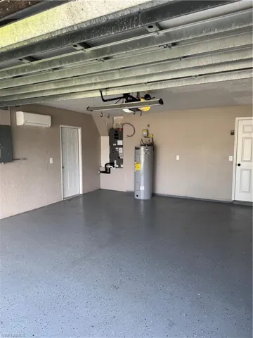 Garage featuring electric water heater, electric panel, an AC wall unit, and heating unit