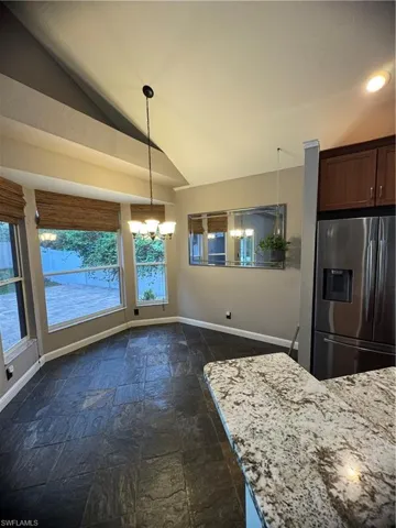 Kitchen featuring refrigerator, stone tile floors, vaulted ceiling, light stone counters, and a chandelier
