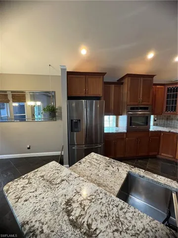 Kitchen with stainless steel refrigerator with ice dispenser, wall oven, light stone countertops, tasteful backsplash, and glass insert cabinets