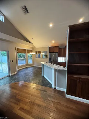Kitchen featuring vaulted ceiling, refrigerator, pendant lighting, dark wood finished floors, and light stone counters