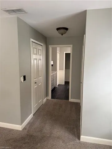Hall featuring dark colored carpet and baseboards