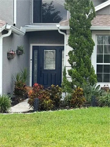 View of exterior entry with stucco siding, a yard, and roof with shingles
