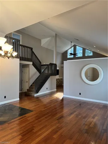 Unfurnished living room featuring hardwood / wood-style flooring, high vaulted ceiling, ceiling fan, and stairs