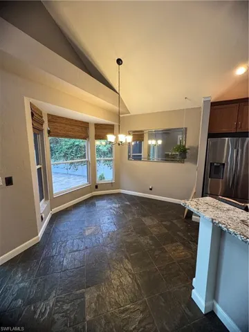 Unfurnished dining area featuring stone tile flooring, vaulted ceiling, and a chandelier