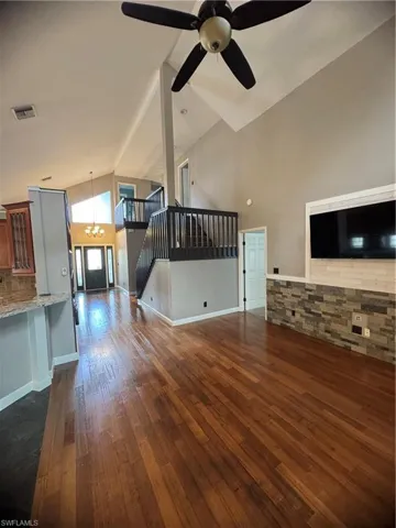 Unfurnished living room featuring high vaulted ceiling, stairs, dark wood-type flooring, a chandelier, and a ceiling fan