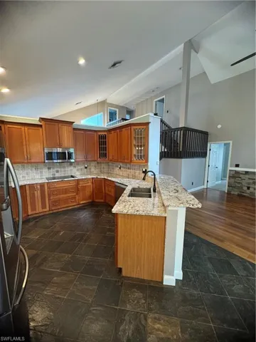 Kitchen featuring vaulted ceiling, a peninsula, brown cabinets, decorative backsplash, and glass insert cabinets