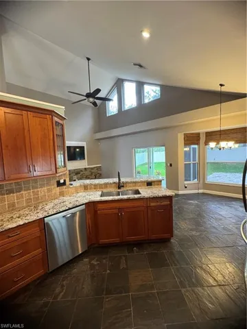 Kitchen featuring high vaulted ceiling, brown cabinets, a peninsula, dishwashing machine, and decorative backsplash