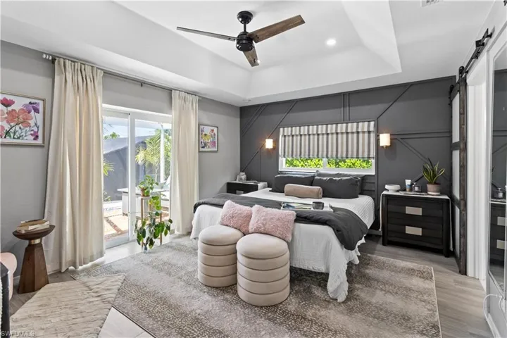 Bedroom featuring light wood-style flooring, a raised ceiling, a barn door, ensuite bath, and a ceiling fan
