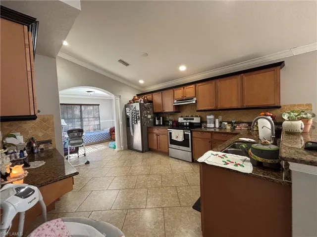 Kitchen featuring arched walkways, brown cabinetry, stainless steel appliances, dark stone counters, and tasteful backsplash