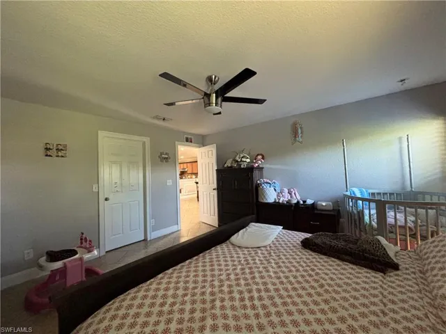Bedroom with a nursery area, a textured ceiling, and ceiling fan