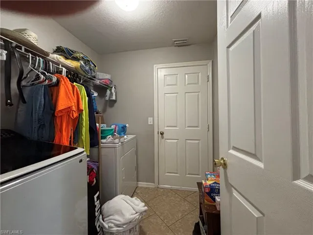 Laundry area featuring a textured ceiling, light tile patterned floors, and independent washer and dryer