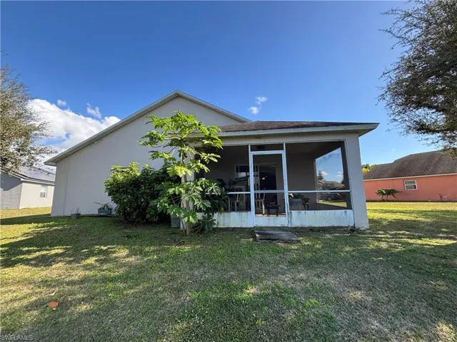 Rear view of house with a sunroom, a lawn, and stucco siding