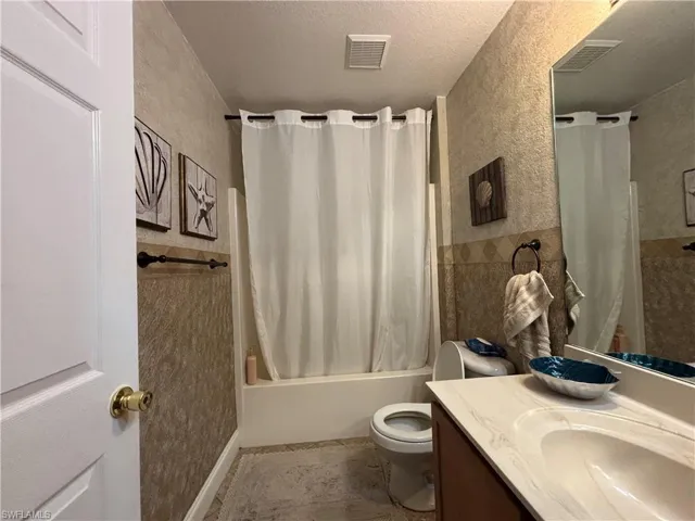 Bathroom with a textured ceiling, shower / bath combination with curtain, vanity, and a textured wall