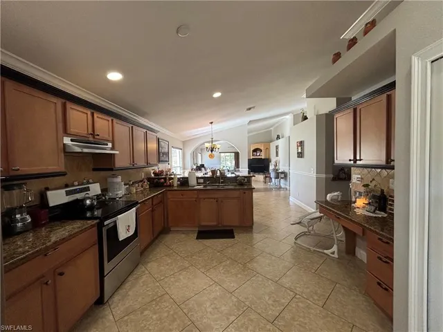 Kitchen with lofted ceiling, stainless steel electric range oven, a peninsula, decorative light fixtures, and dark stone counters