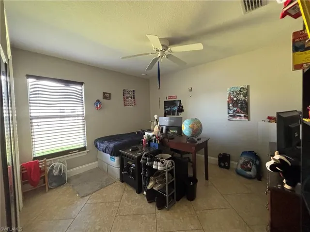 Bedroom with ceiling fan, light tile patterned floors, and a textured ceiling