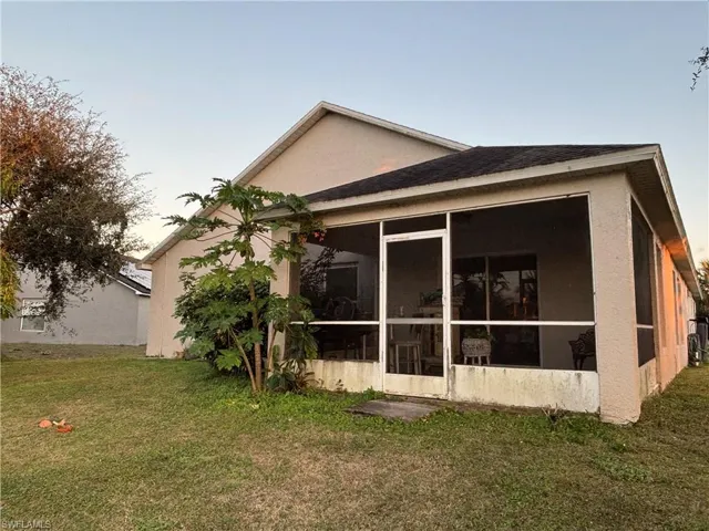 Rear view of property featuring a yard, a sunroom, and stucco siding