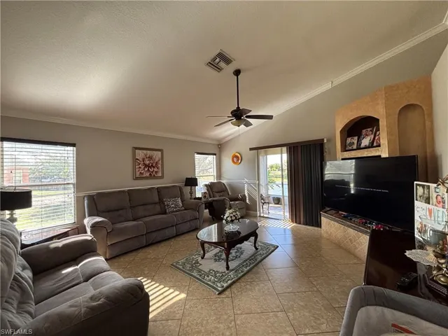 Tiled living area with ornamental molding, lofted ceiling, ceiling fan, plenty of natural light, and a textured ceiling