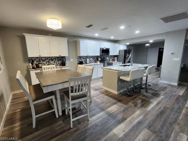 Kitchen with appliances with stainless steel finishes, dark hardwood / wood-style flooring, white cabinets, and a kitchen island with sink