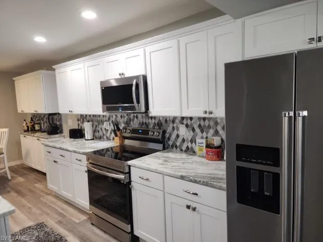 Kitchen featuring tasteful backsplash, stainless steel appliances, white cabinets, light stone countertops, and light hardwood / wood-style flooring