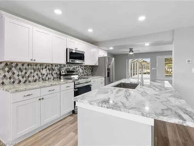 Kitchen featuring tasteful backsplash, light wood-type flooring, ceiling fan, appliances with stainless steel finishes, and sink