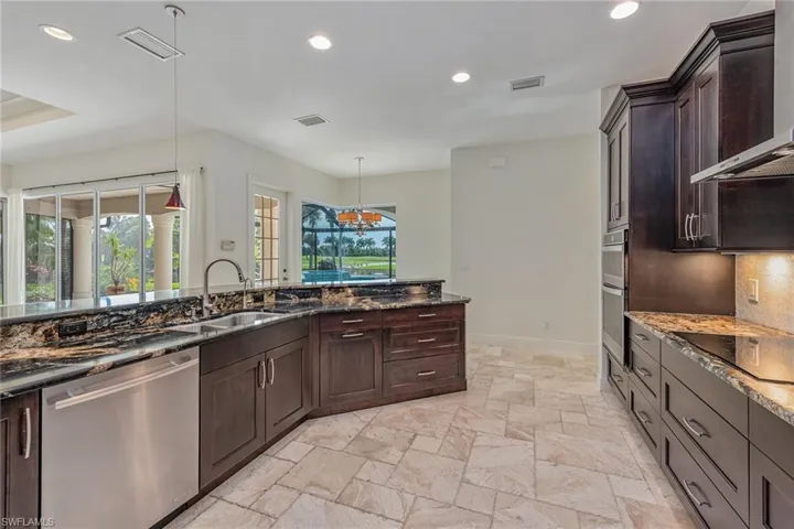 Kitchen with dark brown cabinets, dark stone counters, recessed lighting, appliances with stainless steel finishes, and wall chimney range hood