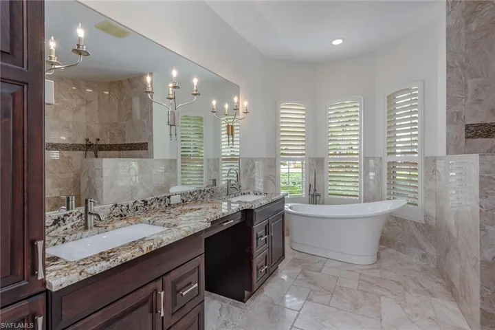 Full bath with a marble finish shower, double vanity, tile walls, plenty of natural light, and a freestanding bath