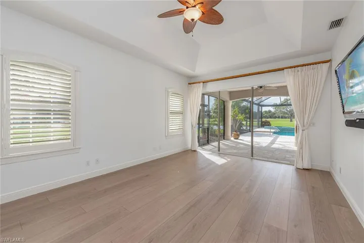Unfurnished room featuring a sunroom, a raised ceiling, light wood finished floors, and a ceiling fan