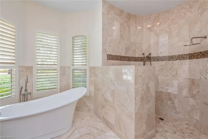 Full bathroom featuring walk in shower, tile walls, a freestanding bath, marble finish floors, and a wainscoted wall