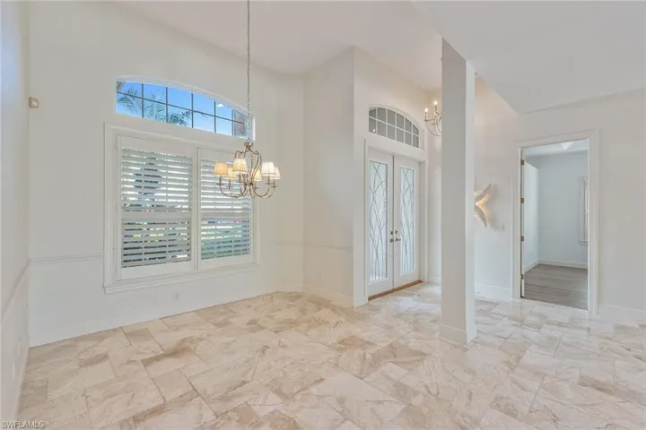 Entrance foyer with french doors, a chandelier, light stone finish floors, and a high ceiling