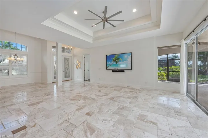 Unfurnished living room with healthy amount of natural light, ceiling fan, a raised ceiling, a chandelier, and recessed lighting