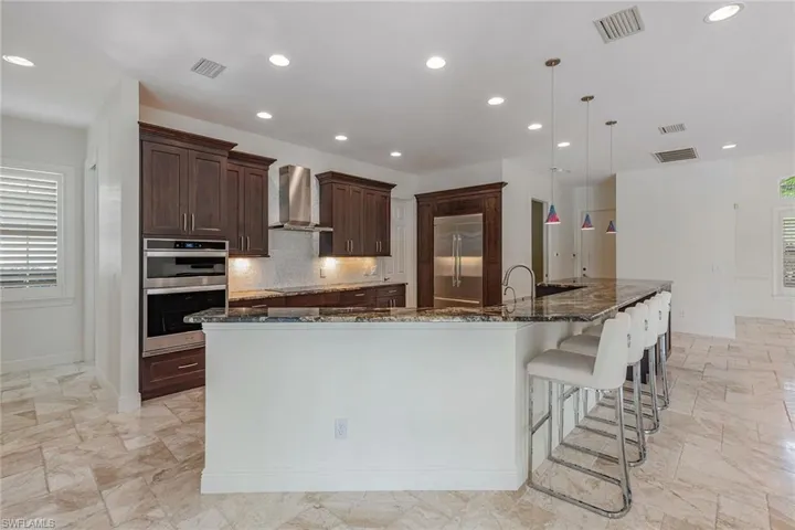 Kitchen featuring dark stone counters, stainless steel appliances, wall chimney exhaust hood, tasteful backsplash, and hanging light fixtures