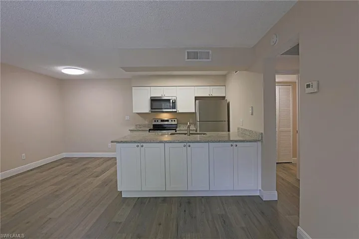 Kitchen with white cabinetry, dark wood-type flooring, stainless steel appliances, light stone counters, and a peninsula