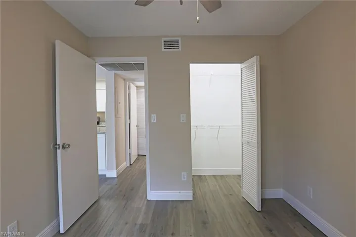Unfurnished bedroom with dark wood-style flooring, a walk in closet, and a ceiling fan